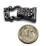 A small ornate dark metallic jewelry clasp, , shown above a U.S. dime for size
