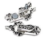 Single-strand magnetic fold over clasp featuring ornate silver metalwork with black enamel accents and swirling decorative details. The strong magnetic closure works together with the hinged fold-over design for added security. Displayed in multiple positions, this bracelet clasp includes one loop at each end and is perfect for bracelet making, jewelry findings, beading projects, and handcrafted jewelry designs.