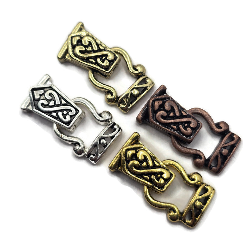 Four ornate Celtic knot metal fold over magnetic clasps pieces in gold, silver, and bronze finishes, arranged diagonally on a plain white background.