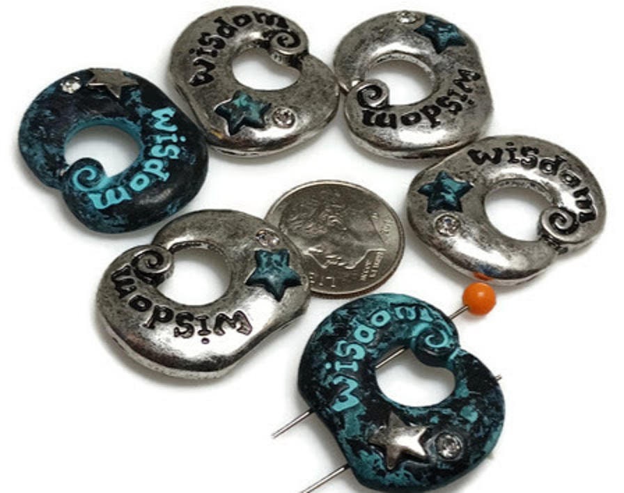 Wisdom donut 2‑hole slider beads with etched text, silver stars, and teal verdigris accents. Mixed finishes—antique silver and turquoise wash—create artistic contrast. Use as bracelet focal, separator, or double‑strand spacer for chokers and cuffs. These beads pair beautifully with pearls, jasper, or crystals, adding meaningful symbolism to boho, spiritual, and inspirational jewelry collections.