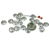 Silver metal beads with a spiral design.  Approximately twenty silver-toned beads are scattered on a white surface, near a US dime for scale. The beads have an open, swirling pattern.  They appear to be small, decorative metal components suitable for jewelry making or crafting.