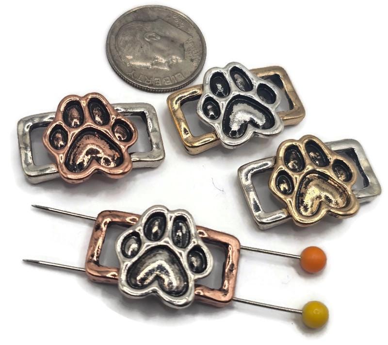 These paw print two‑hole slider beads combine playful meaning with durable design. Each features a raised paw symbolizing love for animals, highlighted in antique silver, copper, and brass colors. Their rectangular frames include dual side holes, offering stability in bracelets, chokers, or double‑strand necklaces. Great for artisan jewelry creators who specialize in pet‑themed keepsakes and handmade memorial gifts.