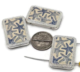 Three rectangular silver-toned pendants with a starfish pattern. The starfish are navy blue on a cream background. The pendants have a silver-toned beaded border. A dime is next to the pendants for size comparison. The pendants are on a white surface.