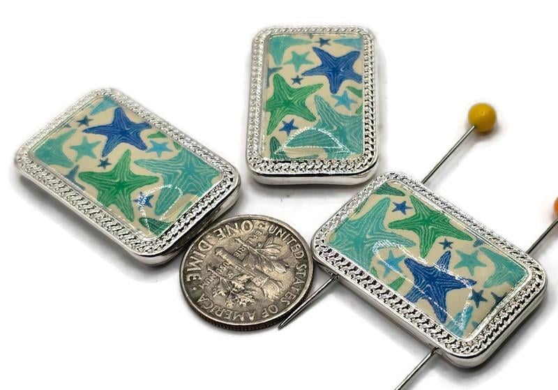 Ocean‑themed rectangular 2 hole slider beads with bright silver frames and glossy panels of blue and teal starfish. Perfect focal sliders, spacers, and connectors for bracelets, chokers, and necklaces using duo beads, SuperDuo beads, or twin duo beads alongside seed beads as filler beads. Pair with pearls, crystals, or sea‑glass colors for coastal designs. Essential metal beads, spacer/connector components, and jewelry findings for summer collections, DIY kits, and small‑batch wholesale.
