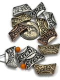 A collection of decorative metal beads in various metallic finishes, including silver, gold, and copper. The beads have a rectangular shape with a curved design and intricate etched patterns. Some beads are strung on a wire with orange beads. A dime is included for size comparison.