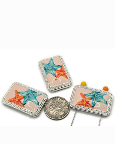 Starfish sea‑life 2 hole slider beads with a peach enamel panel framed in bright silver. The watercolor blue and coral‑orange starfish create an instant beach focal for bracelets, chokers, and necklaces. Use these metal beads as slider focals, spacers, or connector components; frame with seed beads as filler beads and add pearls or crystals for shimmer. Perfect jewelry making supplies and beading components for summer collections, beach weddings, vacation gifts, and small‑batch wholesale.
