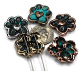 Paw print shaped beads with a heart in the center. The beads are in various colors including silver, gold, copper, and turquoise. A dime is placed in the center for size comparison. The beads have holes for stringing.