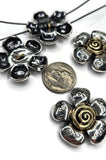 Silver flower pendants with gold centers. The pendants are in a floral design with petals and a spiral center. One pendant has the word 'Hope' engraved on the petals. A dime is next to the pendants. The pendants are on a white surface.