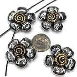 Four silver-colored flower charms with gold-colored spiral centers. Each flower has five petals with the words 'Love', 'Wish', 'Hope', and 'Faith' etched on them. A dime is placed near the charms for size comparison.