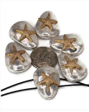 A collection of silver-colored, oval-shaped beads, each adorned with a gold-colored starfish. A dime is placed in the center for size comparison. The beads are connected by a black string, suggesting they are intended for jewelry making. The starfish design is a prominent feature.