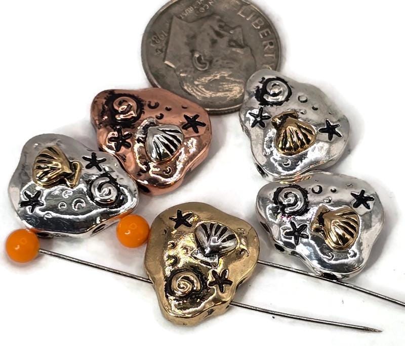 Celebrate seaside style with these pebble‑shaped seashell beads. Each bead highlights a detailed raised shell, spiral accents, and tiny stars, finished in antique copper, brass, and silver. Dual‑hole construction keeps them aligned, ideal for bracelet focals or necklace pendants. Lightweight yet durable, they’re artisan supplies perfect for nautical jewelry, summer gifts, or boho designs inspired by the ocean.