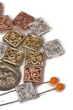 These elegant square filigree 2 hole slider beads feature intricate swirling scroll designs in mixed metallic finishes of silver, copper, and bronze-gold. Their detailed pattern and shiny finish make them versatile enough for bracelets, necklaces, pendants, or chokers. With a secure two-hole slider construction, these beads sit flat, adding both decorative beauty and stability to multi-strand projects. Perfect as focal beads or spacers.