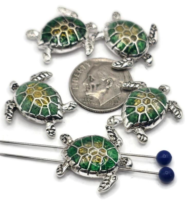 These sea turtle slider beads are perfect for coastal-inspired jewelry designs. Each bead features a silver-tone frame with a vibrant green and yellow enameled shell, capturing the beauty of the ocean. The dual 2-hole slider construction ensures strands remain flat and secure, making them ideal for chokers, bracelets, and necklaces. Perfect for boho artisans, nautical jewelry, and handmade gifts for beach lovers.