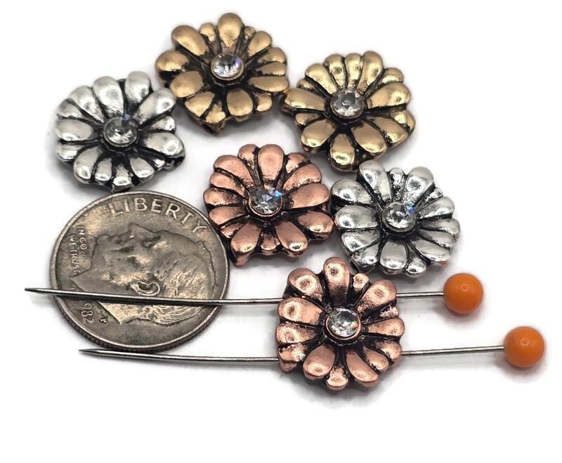 These sparkling daisy 2‑hole slider beads shine in three reflective finishes—silver, copper, and gold—each with a clear crystal centerpiece. Their layered petals and dual threading make them perfect for double‑strand jewelry. Ideal for floral, feminine, and bohemian designs, they bring lively texture and brilliance to handmade bracelets and necklaces.