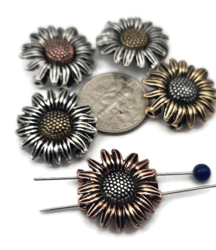 These sunflower 2‑hole slider beads bring rustic elegance to jewelry design. Available in antique silver, brass, and copper finishes, the non‑tarnish coating ensures long‑lasting shine. Their bold, detailed petals and textured center make them perfect as pendants or focal beads in necklaces and chokers. Durable, artisan‑style components ideal for statement jewelry or handmade bohemian pieces celebrating nature’s charm.