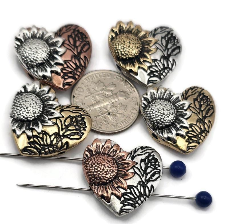 These sunflower heart-shaped slider beads are perfect for statement focal jewelry. Crafted with exquisite sunflower detail and floral accents, they’re available in antique copper, silver, and brass finishes designed not to tarnish. Dual holes ensure stability in multi-strand designs, making them versatile for bracelets or pendants. Great for artisan floral jewelry, rustic gifts, or bohemian collections celebrating nature’s beauty.