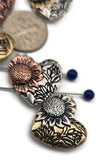 These sunflower slider beads are beautifully designed heart-shaped focals for artisan jewelry. Featuring embossed sunflower motifs and delicate floral accents, they are finished in long-lasting non‑tarnish silver, brass, and copper tones. Crafted with two holes for alignment, they work perfectly as pendants or focal beads in necklaces and bracelets. Great for bohemian, rustic, or floral-themed handmade jewelry designs.