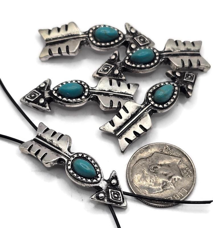 These turquoise arrow slider beads capture Western spirit with engraved arrow details and a vibrant oval centerpiece. Finished in textured antique silver, each bead is crafted with two stringing holes for stability and balance in jewelry. Perfect as focal beads in chokers, pendants, or bracelets, they also make great spacers for layered designs. Ideal for artisans and DIY creators designing boho, tribal, or Southwestern jewelry projects.