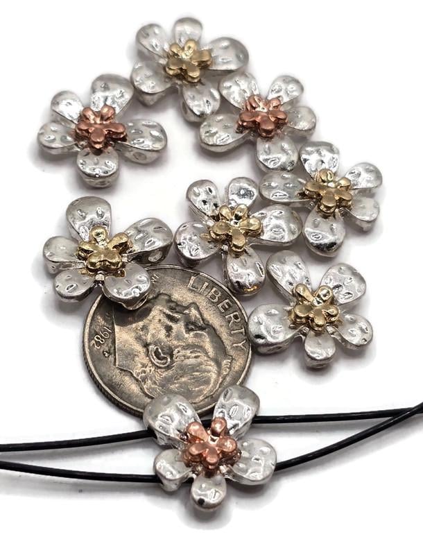 These silver flower 2 hole slider beads feature hammered-style petals with raised copper or gold floral centers. Their two-hole construction keeps beads flat and secure in bracelets, chokers, and necklaces. Perfect as focal beads or spacers, they suit boho, rustic, and romantic jewelry styles. Durable alloy craftsmanship ensures lasting designs for artisans and DIY crafters alike.