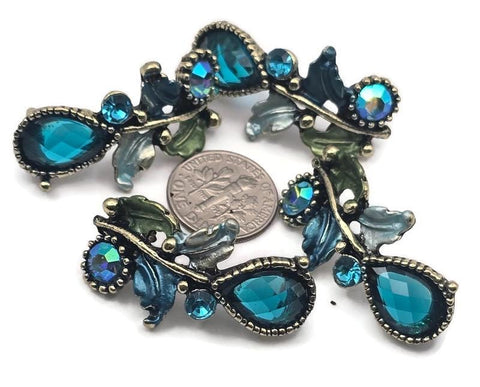 Elevate handmade jewelry with these ornate teal rhinestone 2‑hole slider beads. Faceted pear and round crystals sparkle along antique brass vines with enamel leaves in blue and green. Dual holes keep the focal aligned on bracelets, chokers, or pendant bars. Perfect for statement boho, vintage, or fairytale designs needing rich color, botanical detail, and boutique quality.