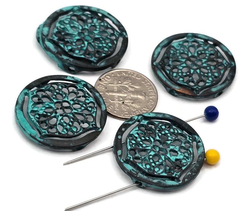 These round filigree 2‑hole slider beads feature a rich turquoise patina over dark antiqued metal, creating an aged, verdigris effect. The lace‑style cutout medallion adds airy detail without bulk. Dual holes keep the focal flat on bracelets, chokers, or pendant bars. Perfect for boho, Southwestern, and vintage designs that need color, texture, and reliable alignment.