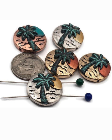 Palm tree sunset beads, 2 hole slider style, in mixed metal finishes. Round coin shape with raised tropical palm, ocean waves, and sun detail. Colors include antique silver, warm copper, and vintage brass with teal patina accents. Great focal beads for bracelet designs and pendants on necklaces. Keywords: beach bead, tropical bead, palm tree bead, sunset bead, coastal jewelry supplies.