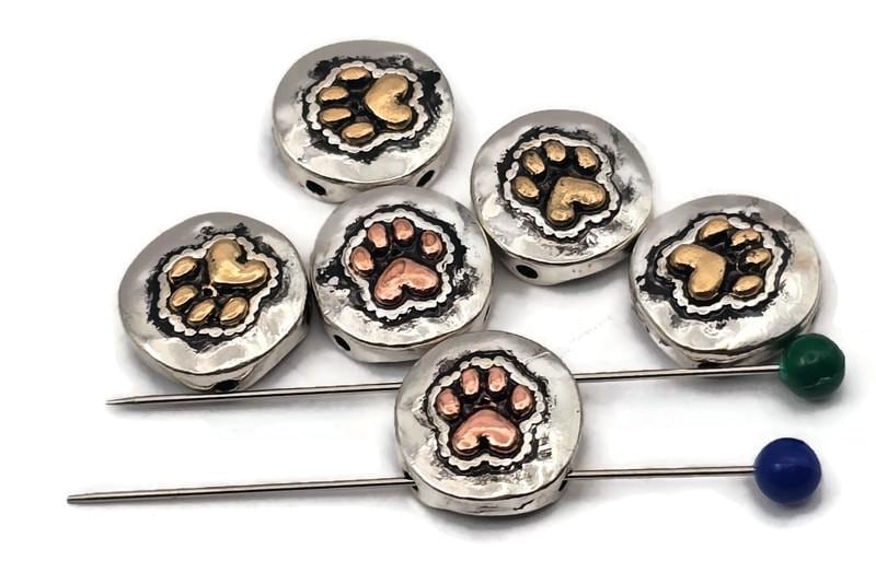 Pet paw print beads, 2 hole slider style, with heart-shaped pads. Round coin face in antique silver with warm copper or brass accents. Textured background adds depth and contrast. Great focal beads for bracelet designs and pendants on necklaces. Keywords: paw print bead, dog cat bead, animal lover bead, pet memorial bead, metal slider bead, pet jewelry supplies.