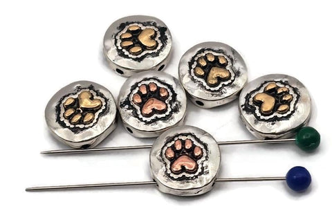 Pet paw print beads, 2 hole slider style, with heart-shaped pads. Round coin face in antique silver with warm copper or brass accents. Textured background adds depth and contrast. Great focal beads for bracelet designs and pendants on necklaces. Keywords: paw print bead, dog cat bead, animal lover bead, pet memorial bead, metal slider bead, pet jewelry supplies.