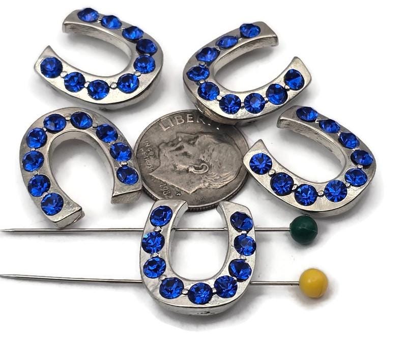 Sparkling horseshoe 2 hole slider beads with vivid sapphire blue crystals in shiny silver metal. Western cowgirl focal beads for lucky bracelets and chokers. Dual, small parallel holes fit fine beading wire, FireLine, or micro cord (not leather). Lightweight, tarnish‑resistant finish. Set of 5 rhinestone horseshoe beads for rodeo, barrel‑racing, and country wedding jewelry.