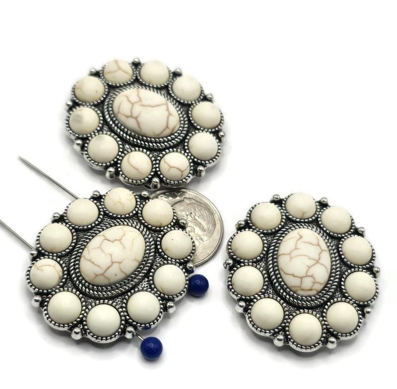 These large oval slider beads are perfect for anyone looking to add elegant Southwestern flair to their jewelry. The detailed silver-tone setting features a white cabochon center, ringed with smaller cabochons for bold dimension. With two side holes for stability, these beads are excellent as statement bracelet focals or centerpiece connectors in multi-strand choker or necklace designs.