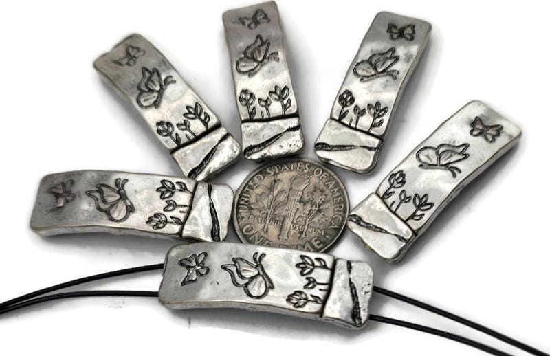 Long rectangle 2‑hole slider beads with etched butterflies and garden flowers. Antique silver finish with gentle curve for wrist comfort. True double‑strand components; two small parallel holes keep thin strands aligned—ideal for 0.015–0.018" beading wire, FireLine, or micro cord. Lovely focal bars for bracelets, chokers, and horizontal pendants. Nature beads for crafting and giftable jewelry.