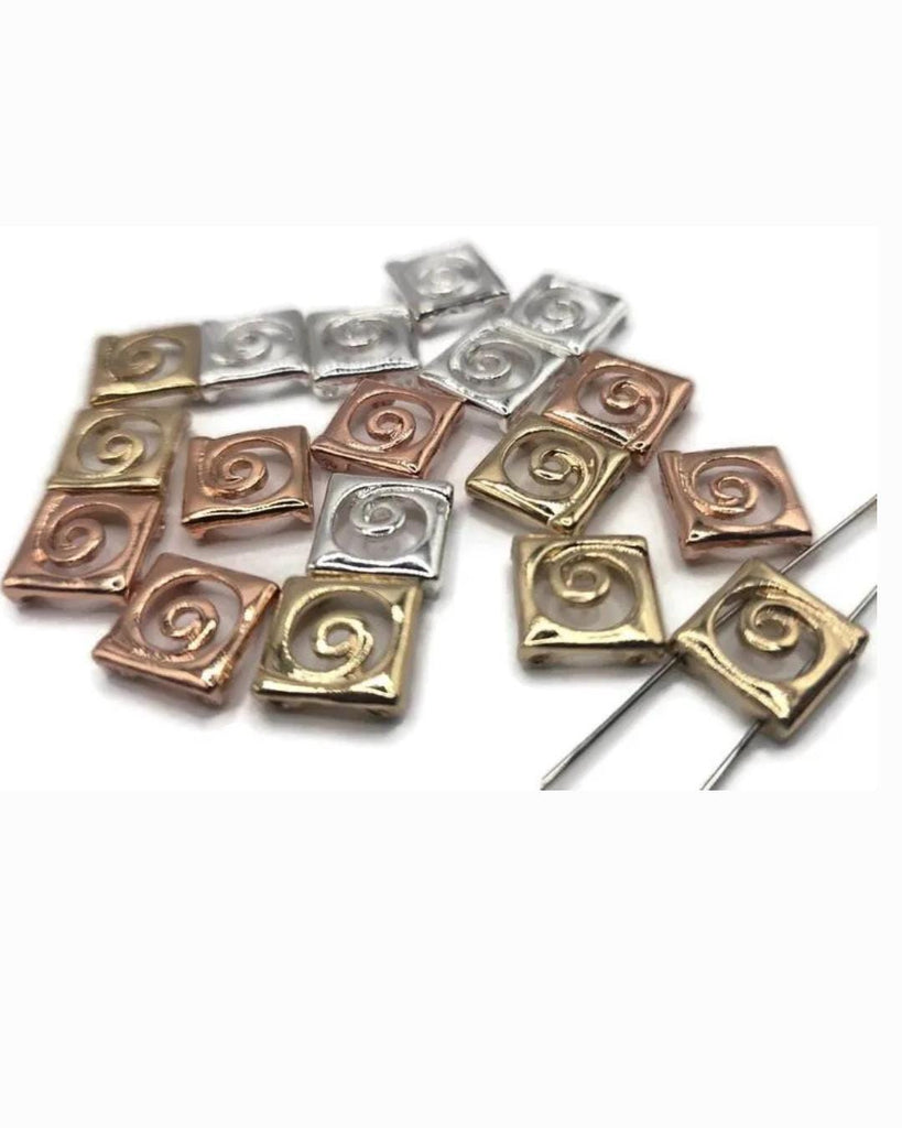 Mixed-metal spiral 2 hole slider beads in silver, gold, and rose copper. Small square pillow beads with raised swirl motif. True slide double‑strand components; small parallel holes fit fine beading wire, FireLine, or micro cord (not leather/chain). Use as focal beads or unique spacer/filler in bracelets, chokers, and necklaces. Jewelry making supplies, components parts, bulk wholesale metal, cheap sliderbeads.