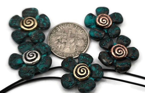 These verdigris flower 2‑hole slider beads feature radiant spiral centers in antique silver, brass, and copper tones. Their teal patina finish highlights engraved details across each petal, creating dimension and depth. Ideal as bracelet focal beads, pendant bar connectors, or double‑strand spacers for artisan and bohemian jewelry styles inspired by nature, renewal, and handcrafted design elegance.
