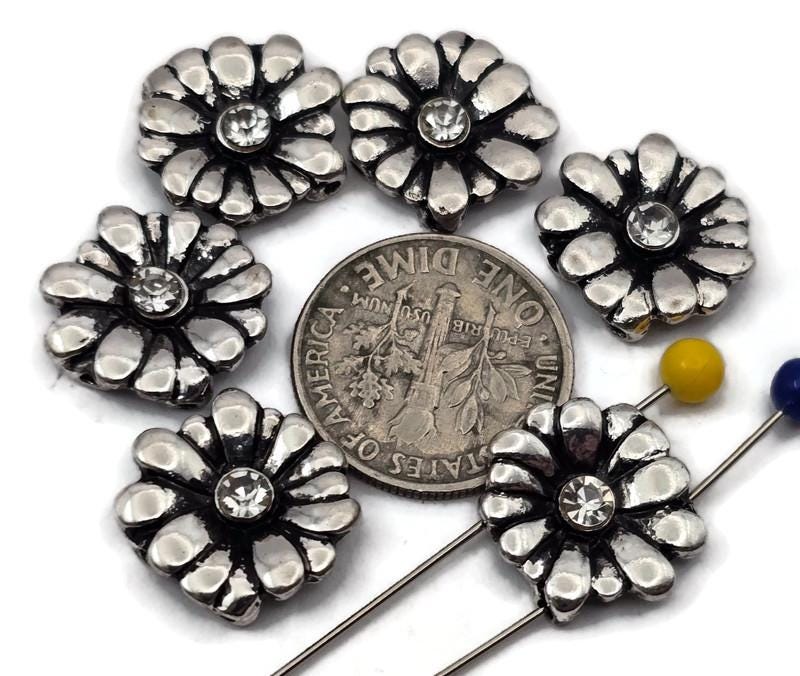 These daisy 2‑hole slider beads feature raised petals surrounding a clear crystal center for a touch of shimmer. The antique silver finish adds depth and vintage charm to bracelets, chokers, and multi‑strand designs. Ideal as focal connectors, double‑strand spacers, or accent beads, they bring refined floral style to bohemian, feminine, and artisan jewelry creations.