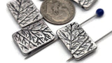 These silver rectangular sliders read like handcrafted metalwork. Intricate tree‑branch artwork on a polished antique finish. Use as focal beads, flat spacers, or centerpiece charms in thin multi‑strand designs. Small holes fit fine wire and thread only. Pair with moss agate, jade, amazonite, or pearls for modern botanical pieces. Pack of five artisan beads.