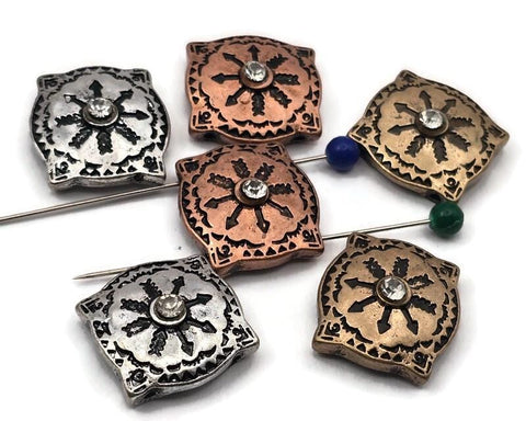 Mixed-metal 2 hole slider beads with an ornate sunburst medallion and a sparkling crystal center. The softly squared profile and engraved borders create rich texture that photographs beautifully. Available in antique silver, warm copper, and vintage brass tones. Unique beads and premium metal findings that make effortless focal beads for artisan jewelry. Durable finish designed to stay bright. Ideal for crafters seeking statement metal beads.