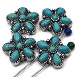 Turquoise cabochon flower beads in an oxidized silver frame. Two parallel holes keep the floral face forward, showing six teardrop petals and a round center with beadwork trim. Rich color and texture make an eye‑catching focal bead for bracelet stacks, chokers, and boho accessories. Western concho‑inspired design with bright turquoise appeal.