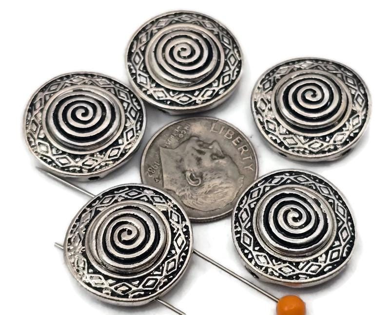 Antique silver spiral 2 hole slider beads with a raised swirl center and geometric border. These round metal beads make easy focal sliders, spacers, or connector components for bracelets, chokers, and necklaces. Frame with seed beads as filler beads; add crystals, gemstones, or heishi for texture. Timeless beading components and findings for boho, tribal, and Southwestern jewelry. Lead and nickel compliant jewelry making supplies for DIY kits and small‑batch wholesale.