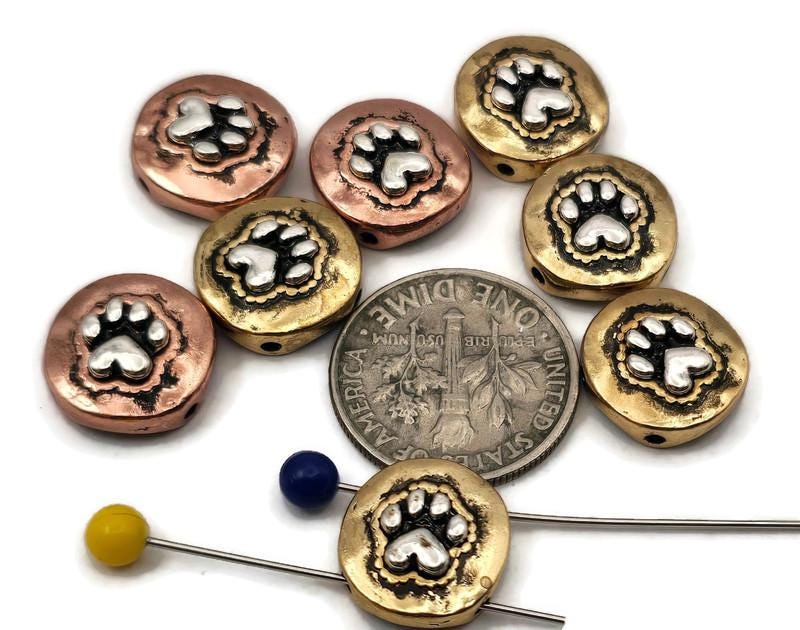 These mixed‑metal paw print 2‑hole slider beads feature raised silver paw designs in antique copper and brass finishes. Perfect for double‑strand bracelets, chokers, or multi‑strand necklaces, they add warmth, contrast, and character to pet‑themed jewelry. Use them as focal beads, spacer bars, or pendant connectors for designs celebrating dog and cat lovers.