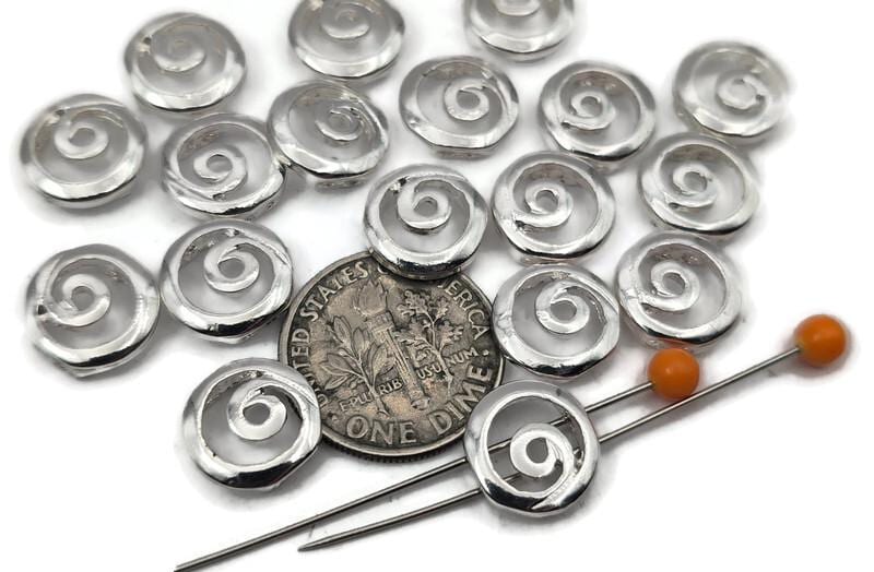 Shiny silver swirl 2 hole slider beads with a smooth domed profile and cutout spiral motif. These round metal beads act as focal sliders, spacers, or connector components for bracelets, chokers, and necklaces. String between seed beads as filler beads for clean spacing, or connect to bead‑woven straps for a flat, durable fit. Pair with pearls, crystals, heishi, and Czech glass. Essential jewelry findings and beading components for minimalist, boho, and modern designs.