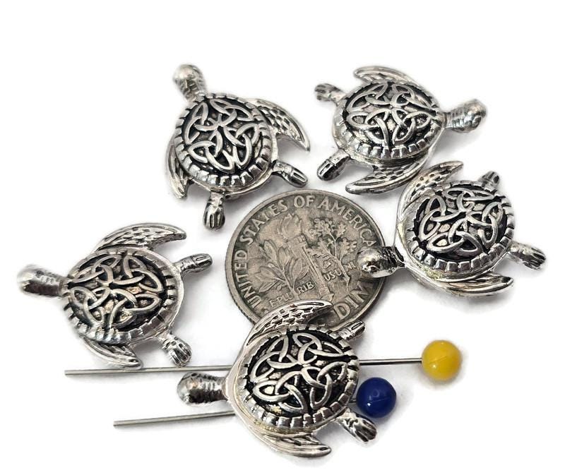 These bright silver sea turtle 2‑hole slider beads feature intricate Celtic knot shells symbolizing unity, harmony, and eternity. With detailed flippers and a polished finish, they align perfectly in double‑strand bracelets, chokers, or necklaces. Durable and beautifully crafted, they’re ideal for coastal, spiritual, or boho jewelry inspired by ocean life and timeless strength.