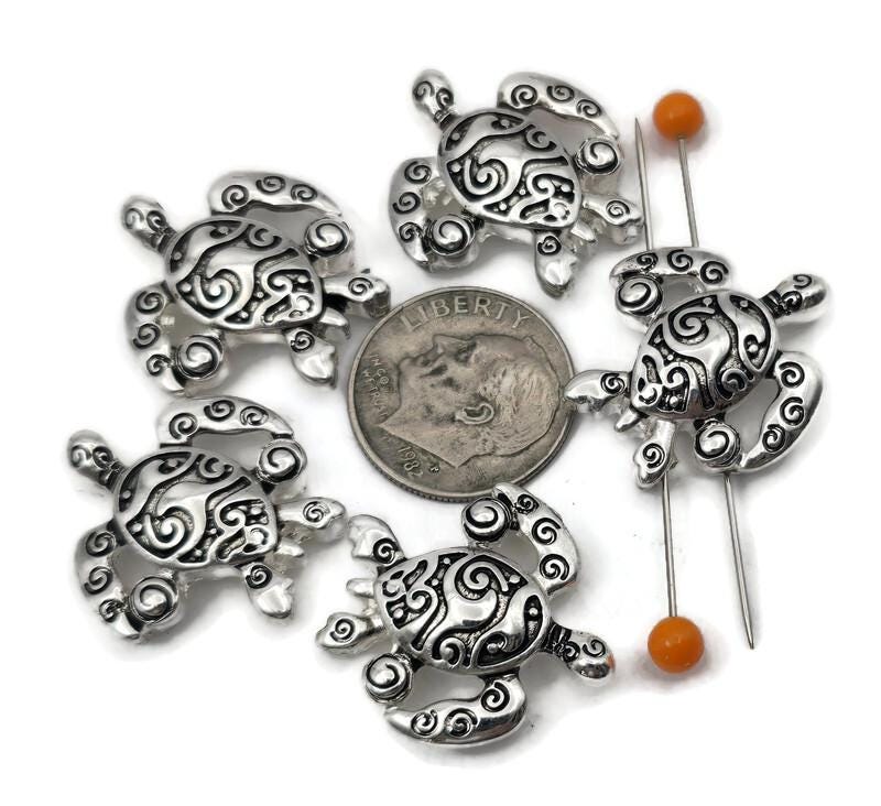 Bright silver turtle 2 hole slider beads for jewelry making, beading, and crafting. These metal beads create an easy ocean focal, spacer, or connector in a bracelet, pendant necklace, or earrings. Pair the sea turtle slider with seed beads as filler beads, beach gemstones (howlite, jasper, amazonite), pearls, crystals, or other metallic beads to finish coastal designs. Fun beading components and findings for summer stacks, gifts, beach weddings, and small‑batch wholesale.