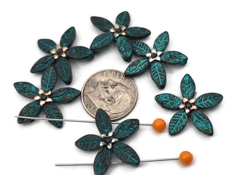 Teal floral 2 hole slider beads for jewelry making and crafting. Each five‑petal bead features leaf‑etched petals with an antiqued teal wash and a tiny metallic center, perfect as a flower focal, spacer, or connector. Build bracelet stacks with seed beads as filler beads, or use a single slider as a pendant connector and earring center. Pairs with gemstones, pearls, crystals, Czech glass, and other metallic beads. Essential beading components and findings for DIY and small wholesale.