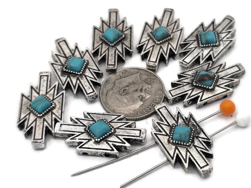 These Southwestern lightning bolt 2 hole slider beads feature a turquoise‑style center set in a bold silver‑tone geometric design. The double‑hole construction keeps two strands aligned, making them perfect focal beads for leather bracelets, chokers, and hatbands. Pair with seed beads, Czech beads, heishi, or gemstone chips for striking Western jewelry. Durable metal bracelet beads and jewelry making components for boho, rodeo, and tribal‑inspired designs.