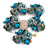 These ornate 2 hole slider beads feature large faceted blue zircon cube stones, smaller blue zircon accents, and decorative enamel leaf details in teal and green tones. Perfect as focal beads for bracelets and chokers, the double‑hole design keeps two strands of leather, cord, or beading wire aligned and centered. Pair with seed beads, Czech beads, and crystal accents for glamorous designs. Beautiful bracelet beads and jewelry making components for boho and statement jewelry.
