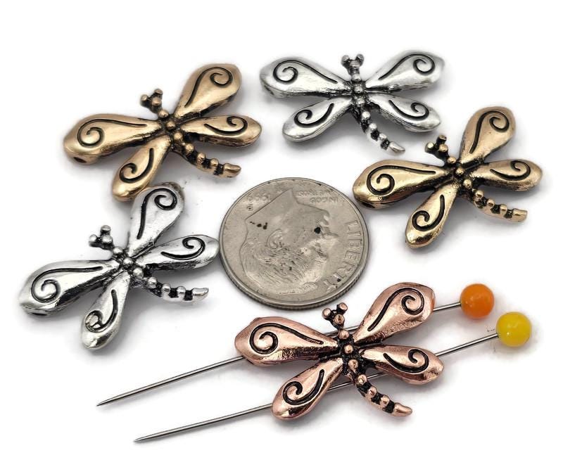 These ornate dragonfly 2 hole slider beads feature scrolled wings and detailed body work in metal finishes. Perfect as focal beads for bracelets and chokers, the double‑hole design keeps two strands of leather, cord, or beading wire aligned and centered. Pair with seed beads, Czech beads, crystals, or gemstone chips for nature‑inspired designs. Beautiful bracelet beads and jewelry making components for boho, garden, and whimsical beading projects.
