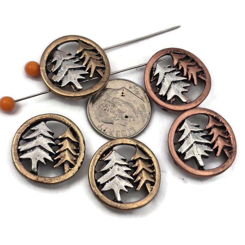 Add rustic woodland charm to your jewelry designs with these two hole pine tree slider beads featuring warm bronze and copper tone frames with layered tree silhouettes. These nature inspired beads are perfect for double strand bracelets and necklaces using leather cord, beading wire, or thread. They pair beautifully with seed beads, superduo beads, Czech glass beads, gemstone beads, and metal spacers for forest jewelry, nature themed accessories, and handmade rustic designs.