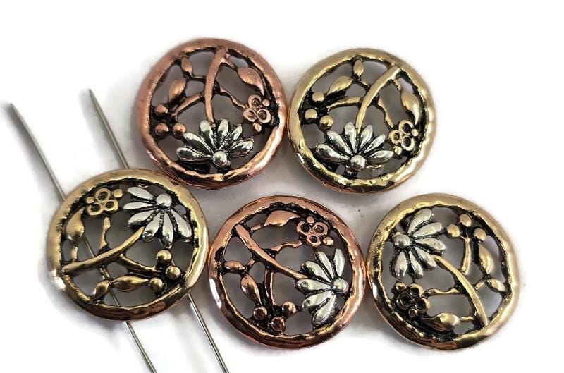 Add vintage style floral charm to your jewelry with these 2‑hole flower slider beads in warm mixed‑metal tones. Each round bead features a raised daisy/flower design with leafy branches and an antiqued finish for beautiful depth. The two-hole connector style keeps strands aligned—perfect for multi‑strand bracelets, cuffs, and necklaces. Pair with seed beads, gemstone beads, or pearls to create elegant handmade jewelry, beading projects, and DIY crafts.