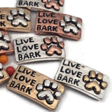 These charming paw print 2 hole slider beads feature the inspirational phrase Live Love Bark with beautiful antique detailing. Designed as metal slide spacer beads for two strand double bracelet necklace designs, they work wonderfully with seed beads, duo beads, and other jewelry spacer components. The mixed metals in silver, gold, and copper make them perfect for dog lover jewelry, pet themed bracelet designs, and creative DIY beading projects.