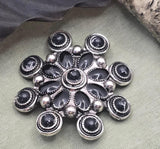 Create eye catching jewelry with these large western floral focal slider beads. The layered design features black enamel accents and antique silver tone detailing in a concho inspired pattern. Perfect for double strand bracelets and statement necklaces, these beads pair beautifully with leather cord, gemstone beads, and metal spacers. Ideal for western jewelry makers, cowgirl designs, and rustic handmade accessories.